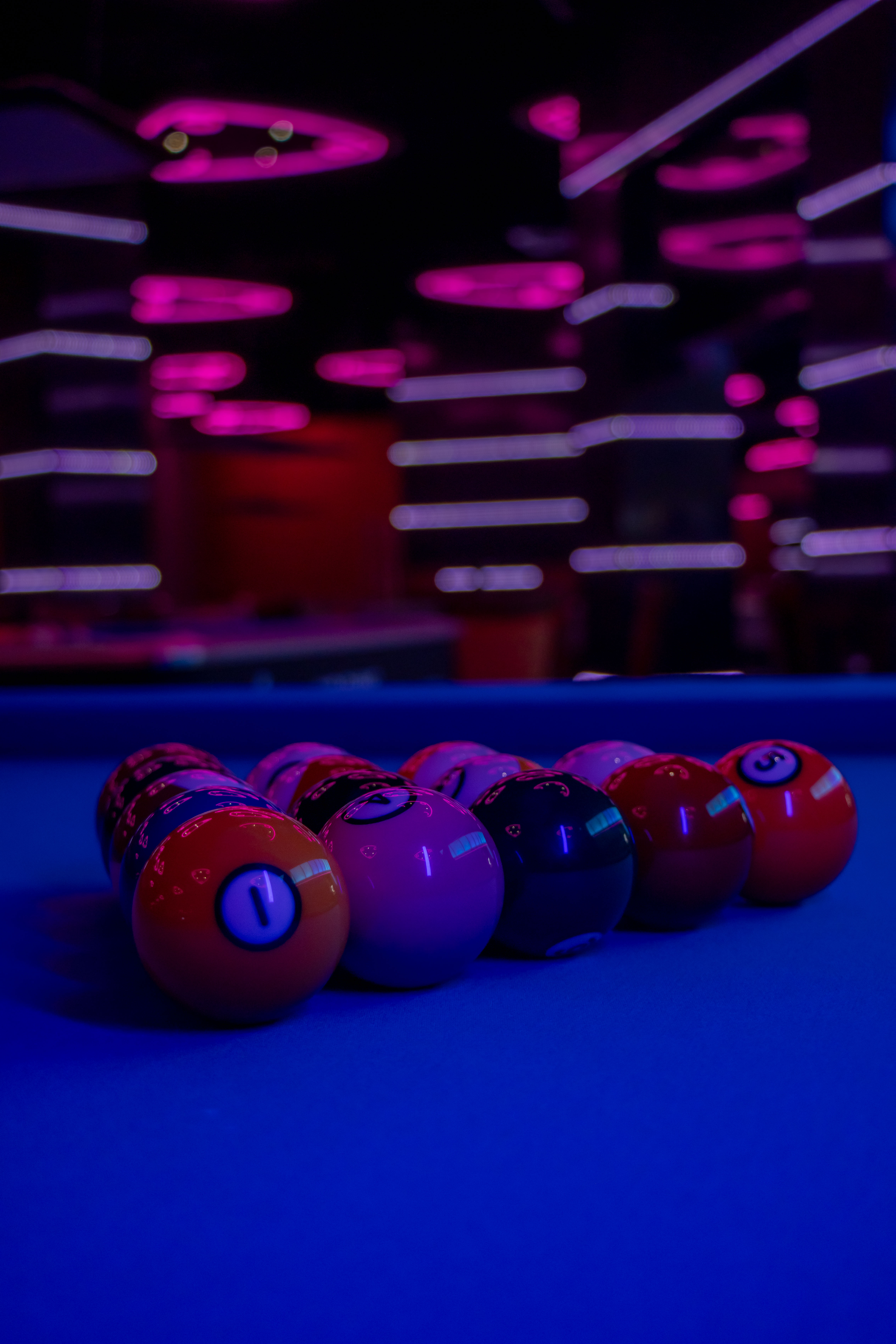 A top-down, artistic shot of a billiard rack on a premium black felt table. The lighting is focused, casting long shadows and highlighting the texture of the balls. The room is dark, creating a high-end, minimalist vibe that feels both technical and luxurious. The composition is centered and perfectly aligned to emphasize precision and order within the Predator club environment.
